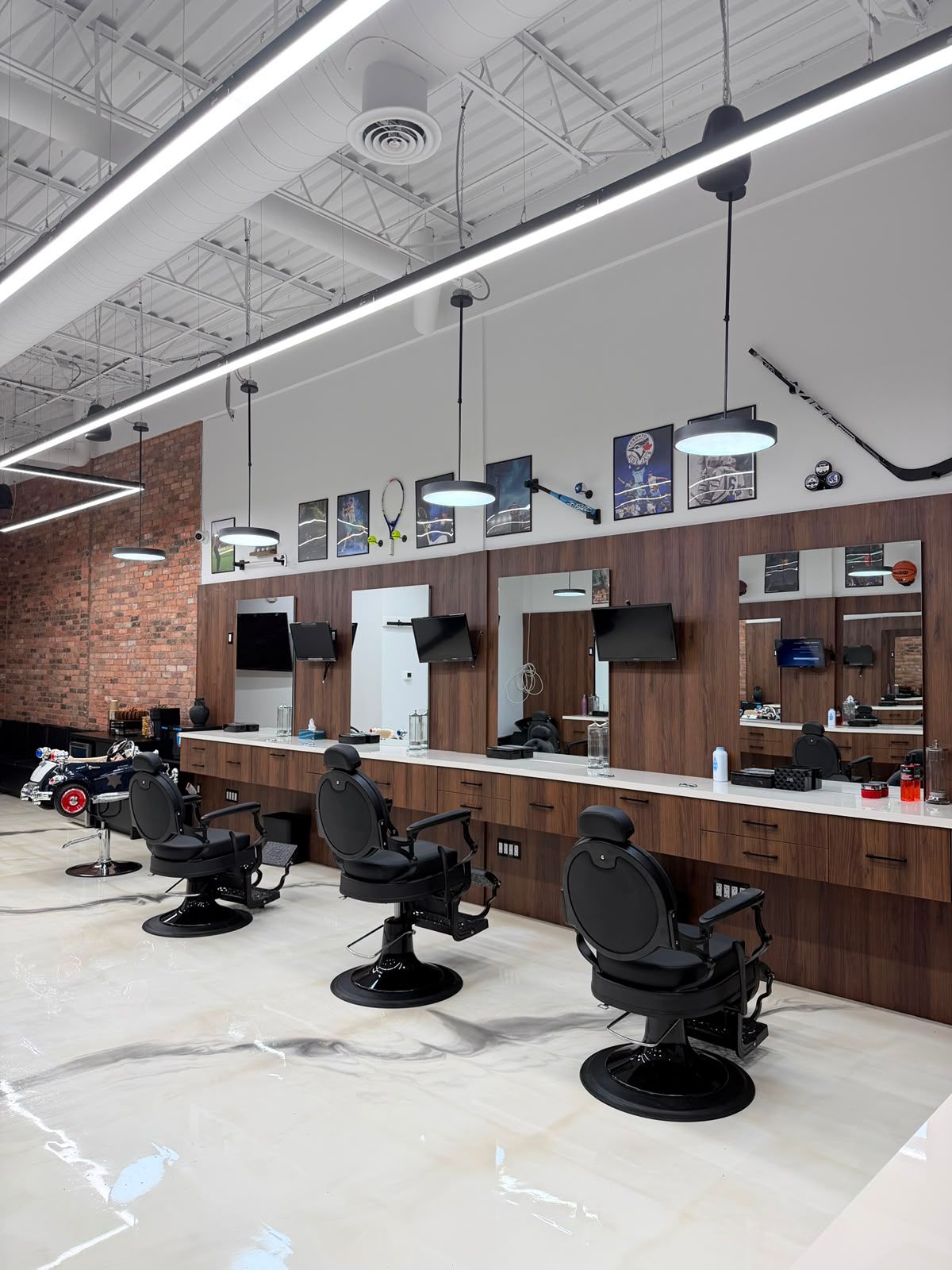 Three black barber chairs lined up at walnut stations with large mirrors, TVs and sports memorabilia at New Legend Barbershop in Hamilton