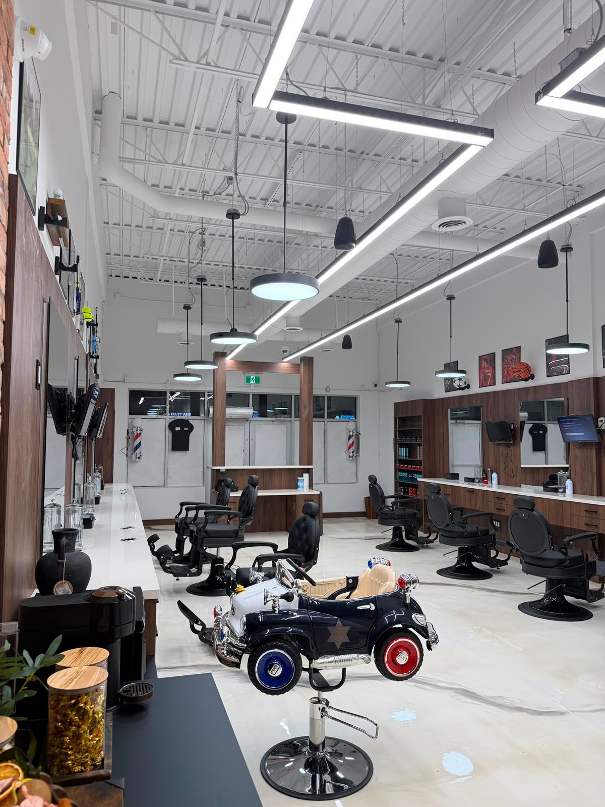 Wide view of the New Legend Barbershop floor in Hamilton with barber chairs on both sides, a barber pole in the front window and a kids' police-car chair