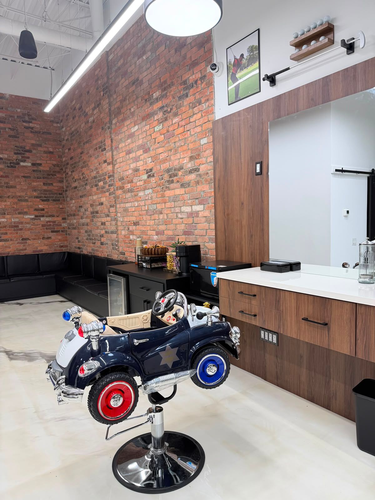 Toy police-car barber chair for kids' haircuts beside the brick-walled waiting area at New Legend Barbershop in Hamilton
