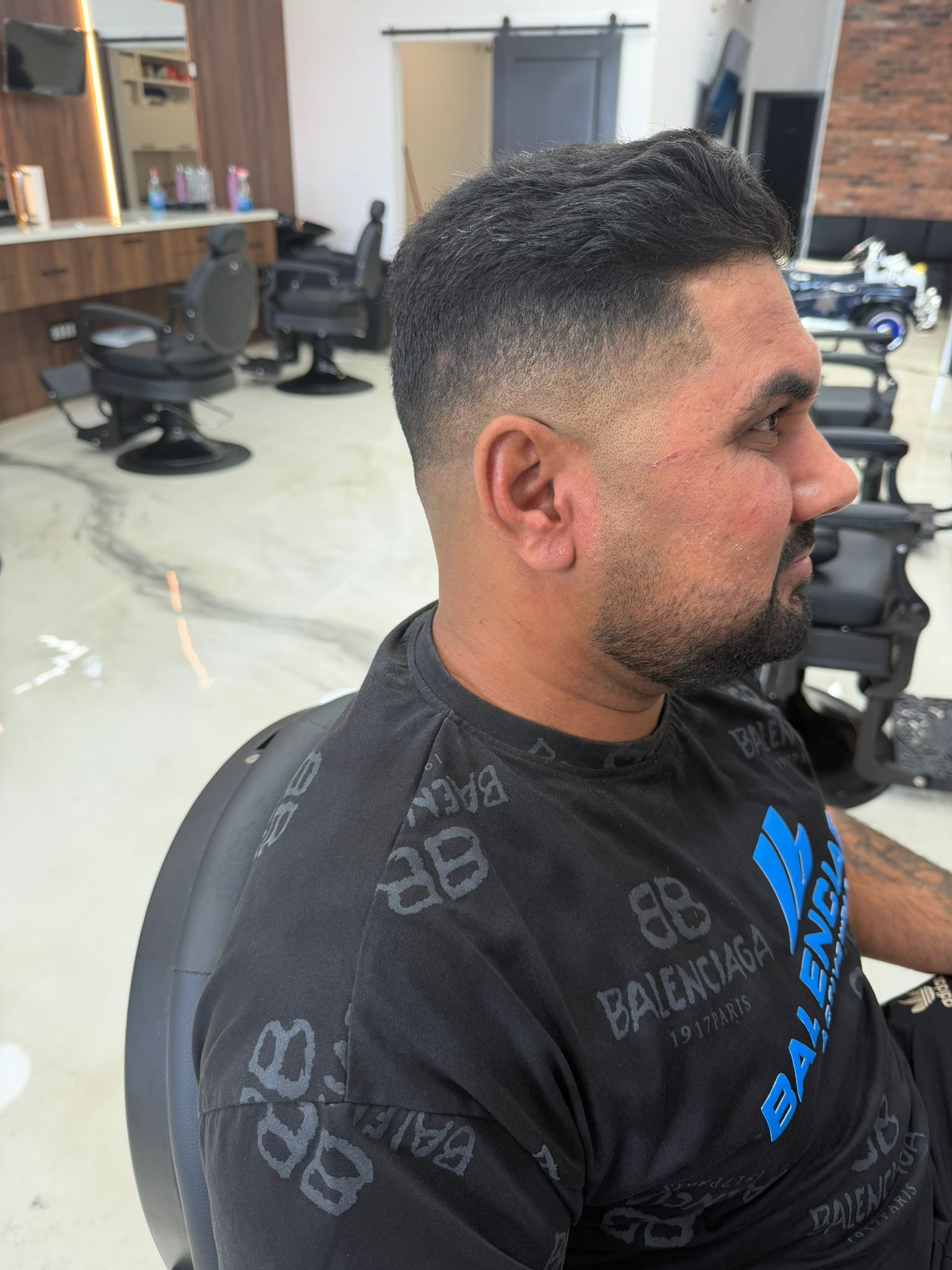 Side profile of a client with a low fade, short textured top and a lined-up beard, at New Legend Barbershop in Hamilton