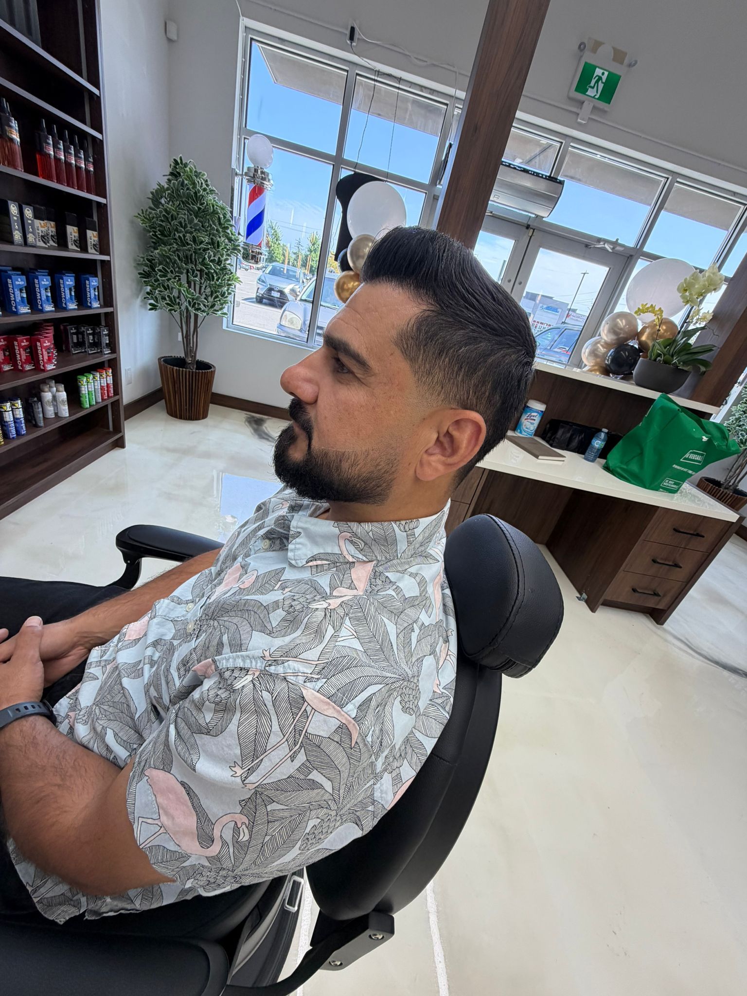Client with slicked-back hair, tapered sides and a full trimmed beard, seated by the front windows of New Legend Barbershop in Hamilton